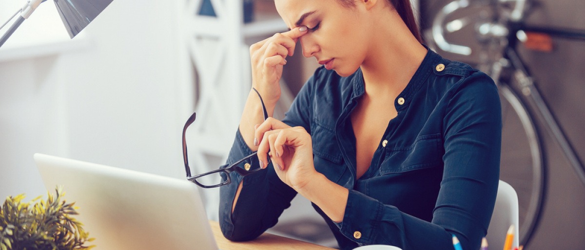 Eine Frau hält eine Brille und reibt im Stress Augen und Nase