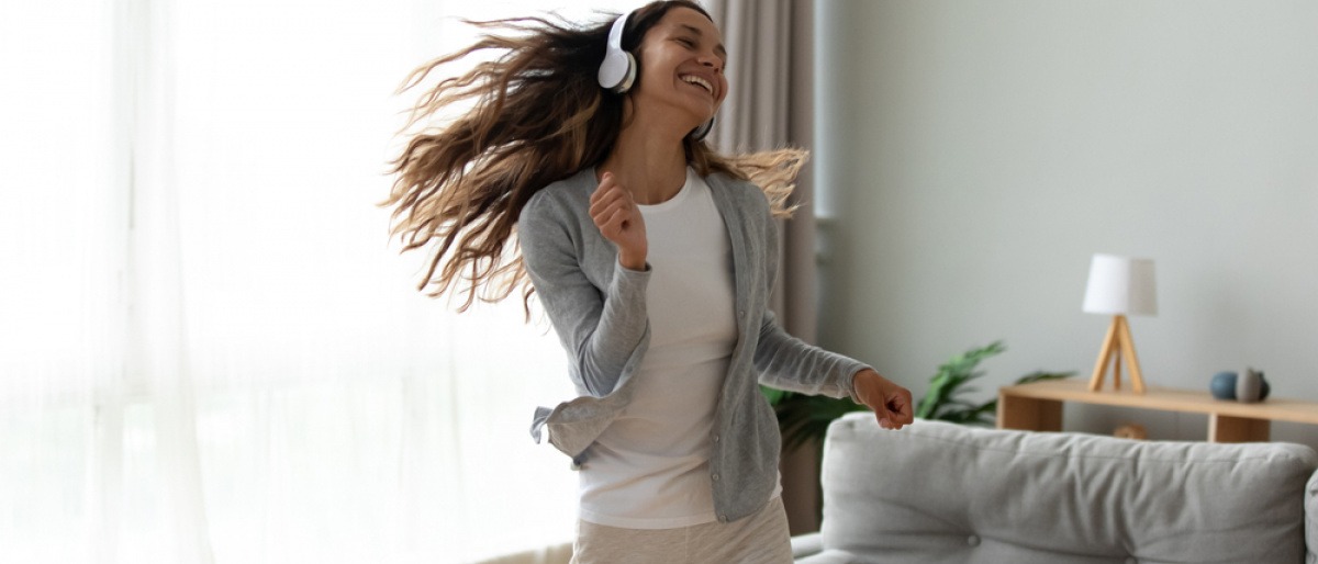 Junge Frau mit Kopfhörern tanzt glücklich im Wohnzimmer