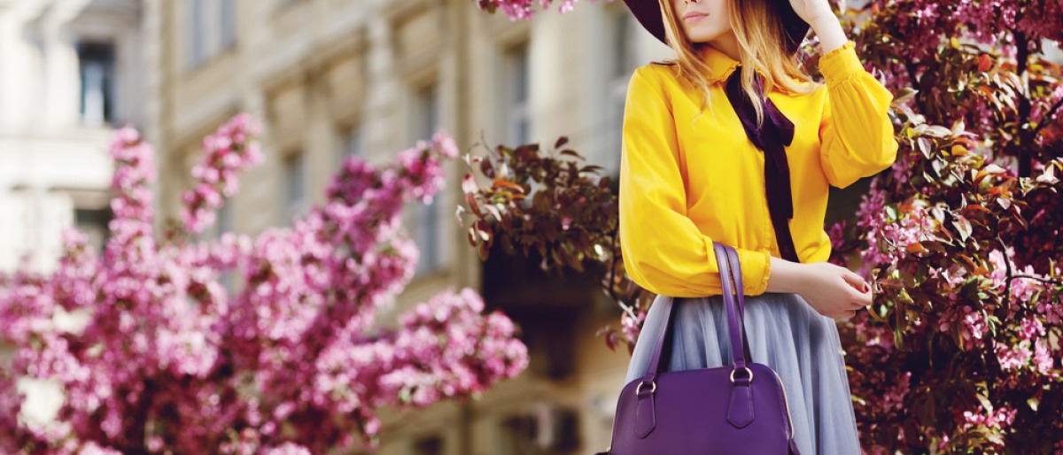 Eine Frau trägt eine tolle trendy frühlingshafte Handtasche in Lila und trägt dabei ein schönes frühlingshaftes Kleid 