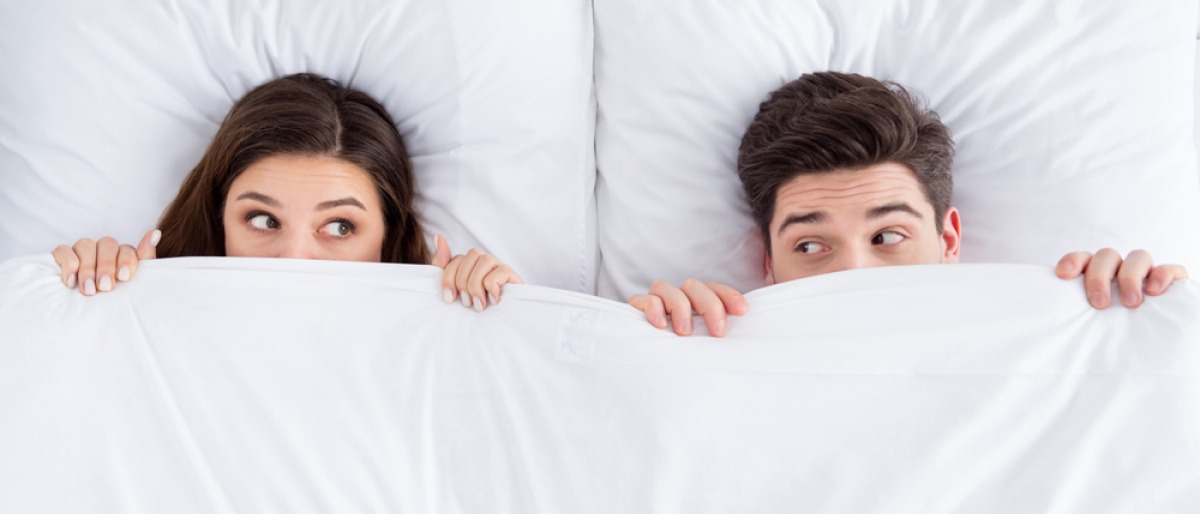 Paar liegt verklemmt im Bett, die Decke bis zum Gesicht gezogen