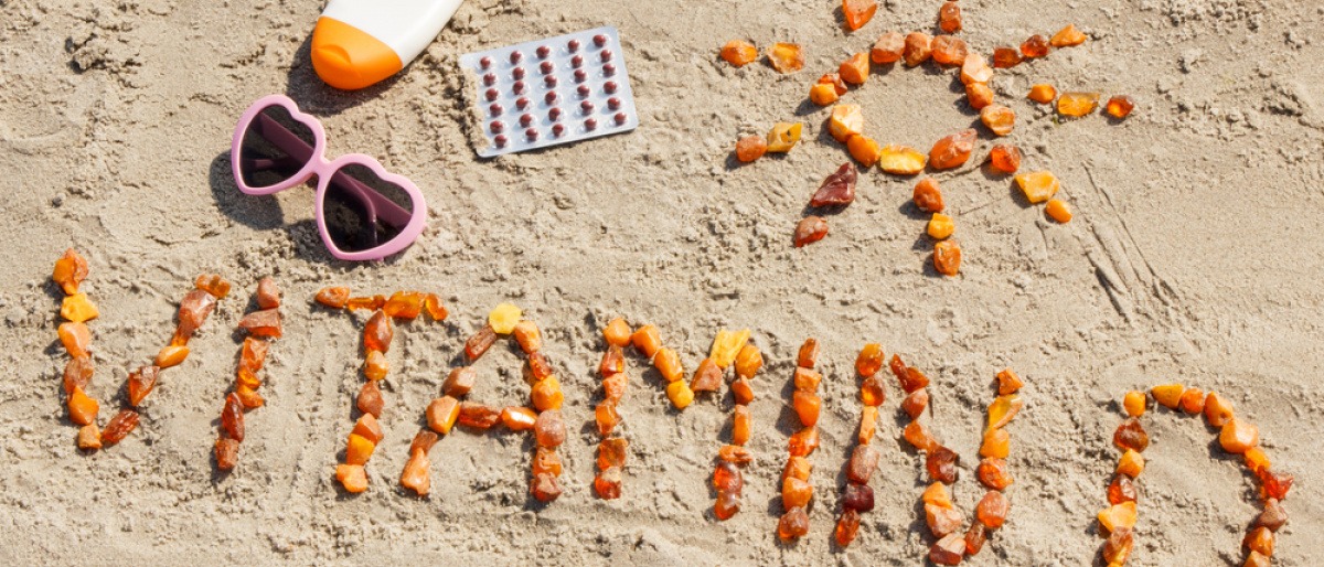 Sonnencreme und Sonnenbrille neben Schriftzug Vitamin D am Strand