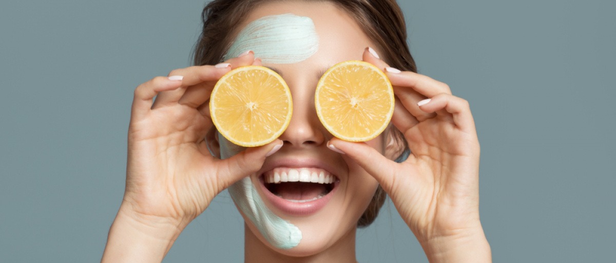 Eine Frau mit Kosmetik im Gesicht hält Vitamine von Orangen als Radikalfänger vor die Augen