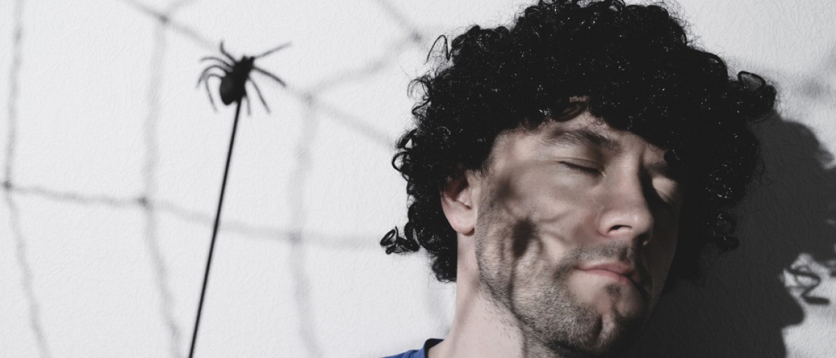 Von Spinnen träumen - träumender Mann hinter einem Spinnennetz mit einer großen Spinne.
