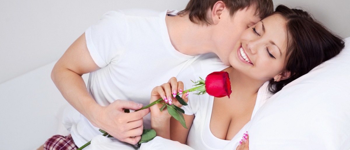 Ein Mann küsst als Vorspiel den Hals einer Frau und hält eine Rose