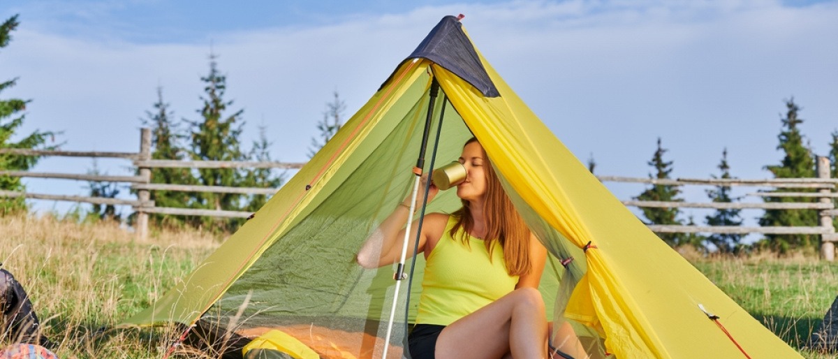 Was braucht man zum Campen? Frau beim Camping im Zelt auf einer offenen Wiese.