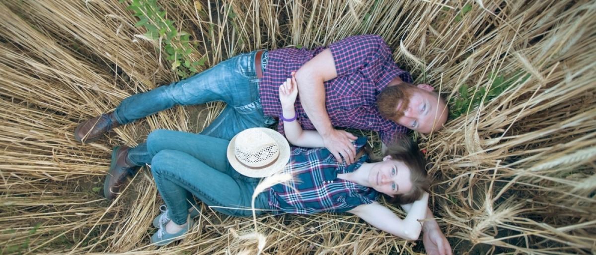 Was macht eine Beziehung aus? Ein glückliches Paar liegt in einem Feld mit hohem Gras und kuschelt.