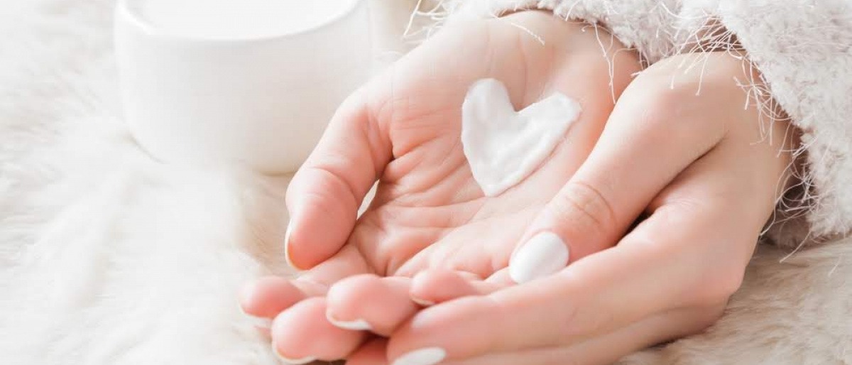 Eine Nahaufnahme der ineinander gelegten Hände einer Frau. Auf der linken Hand liegt ein Herz aus pflegender Creme. 