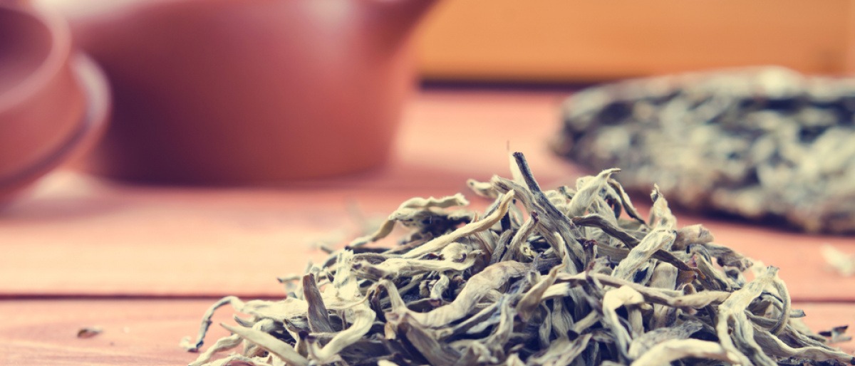 Blätter von weißem Tee liegen neben einer Tasse