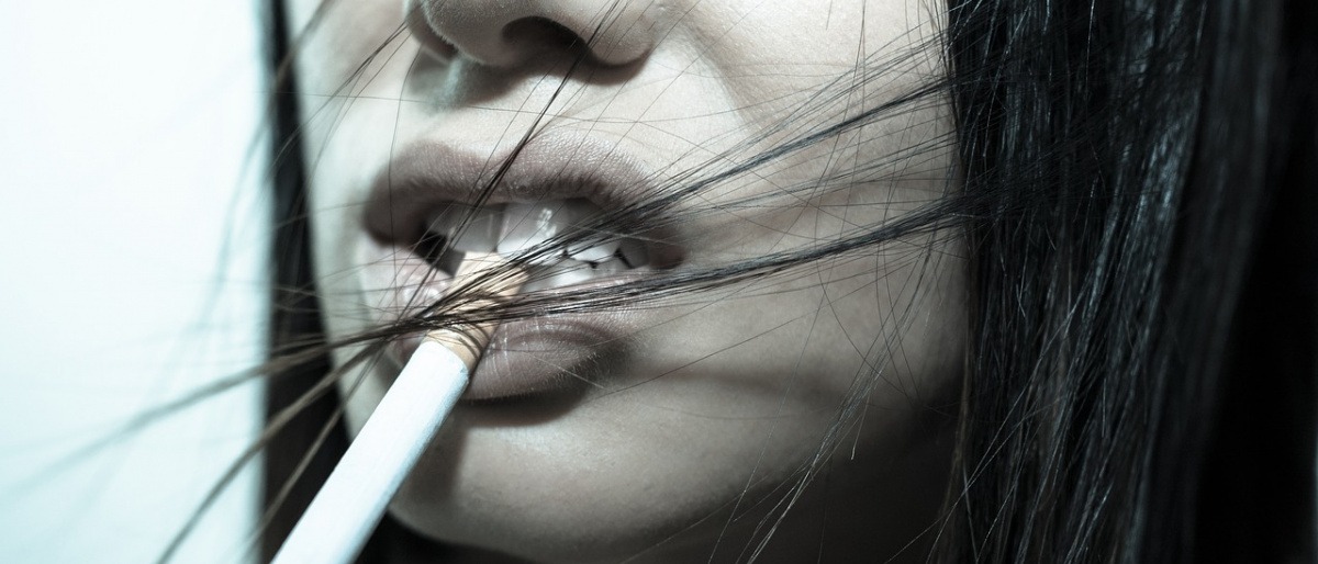 Einer Frau hängt eine Zigarette aus dem Mund
