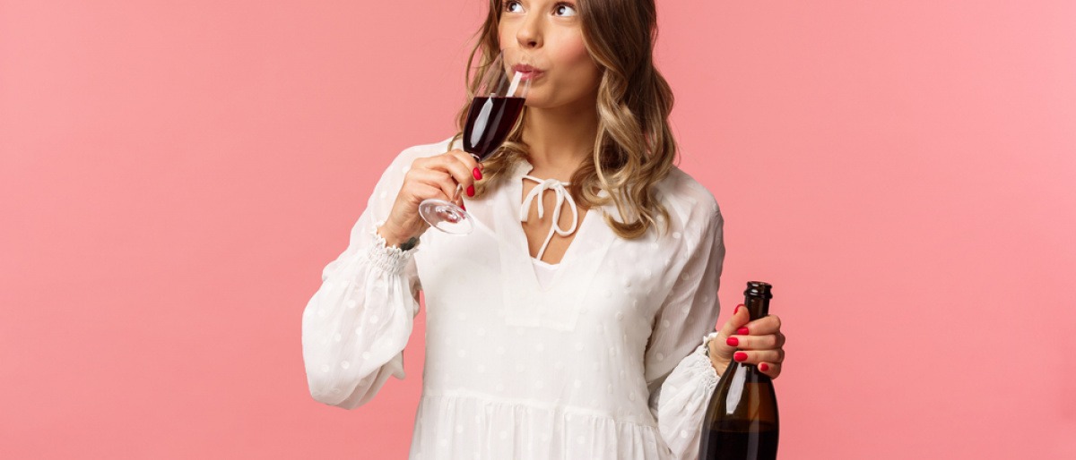 Stehende Frau trinkt Wein und hält die Flasche