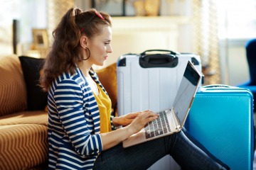 Am Boden zwischen Reisekoffern sitzende Frau arbeitet am Notebook