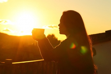 Frau mit Tasse bei einem Sonnenuntergang zum Neumond im Februar 2023