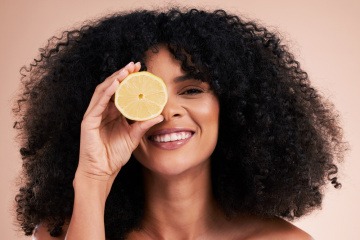 Frau mit schönen Haaren hält eine Zitrone vor ihr Gesicht