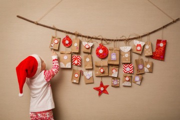 Kind mit Weihnachtsmütze vor selbstgebasteltem Adventskalender.