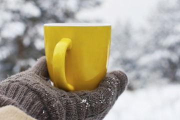Frau mit Hanschuhen im Winter hält Teetasse in der Hand
