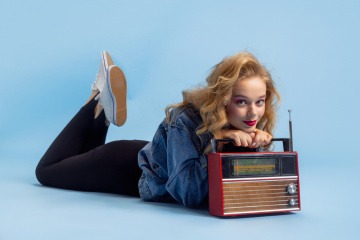 Junge Frau im Stil der 90er-Jahre liegt mit einem Radio auf dem Boden