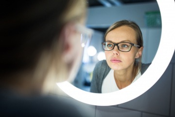 Frau betrachtet im Spiegel ihre Augenringe