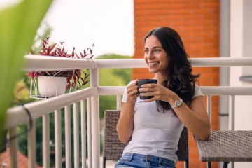 Lächelnde Frau sitzt am Balkon mit einer Tasse Tee