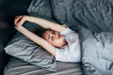 Frau streckt sich im Bett, um ausgeruht in den Tag zu starten