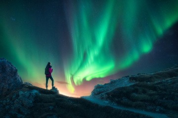 Frau auf einem Berggipfel unter Nordlichtern