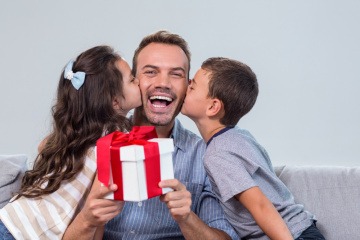 Tochter und Sohn küssen den Vater auf die Wangen, er hält ein Geschenk