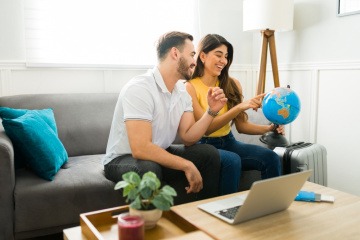 Mann und Frau mit Globus und Laptop bei der Planung eines Reiseziels im Mai