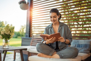 Eine Frau nimmt sich auf der gemütlichen Terrasse eine Auszeit und liest ein Buch