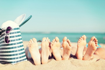 Füße liegen am Strand neben einer Badetasche