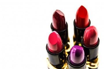 Auf dem Foto sind fünf verschiedene Lippenstifte in Rottönen abgebildet, die in einem Kreis aufgestellt sind