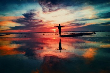 Ein Mensch steht im Sonnenuntergang am Meer und streckt seine Arme aus