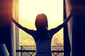 Glückliche Frau beim Öffnen des Vorhangs im Sonnenuntergang.