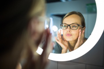 Frau betrachtet ihr Gesicht kritisch im Spiegel
