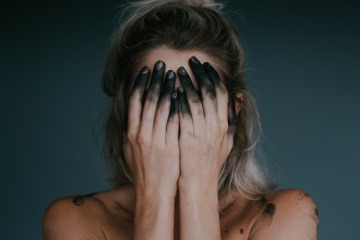 Eine Frau hält sich mit Aktivkohle auf den Händen das Gesicht zu