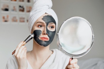 Frau trägt schwarze Gesichtsmaske mit Aktivkohle auf