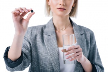 Frau mit einer Tablette Aktivkohle und einem Wasserglas