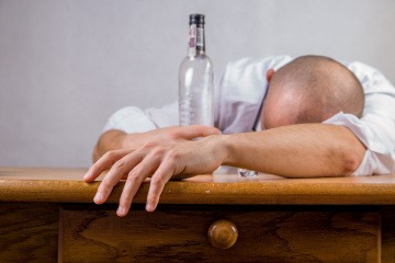 Ein Alkoholiker liegt am Tisch mit einer Flasche in der Hand