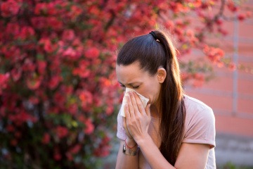 Frau niest vwegen Allergie vor blühendem Busch