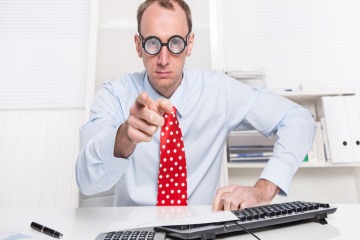 Ein Mann mit Brille und Krawatte sitzt im Büro und zeigt mit dem Finger nach vorne