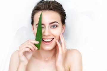 Eine Frau hält ein Aloe Vera Blatt vor ihre Haut
