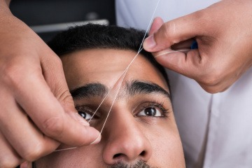 Bei einem Mann werden die Augenbrauen mit Faden gezupft