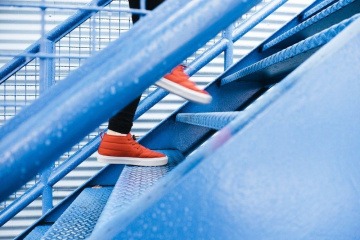 Ein Mensch mit orangefarbenen Schuhen geht eine Außentreppe aus Stahl nach oben