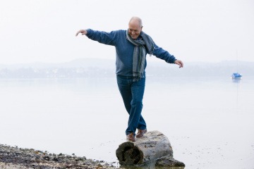 Ein älterer Mann balanciert auf einem Baumstamm