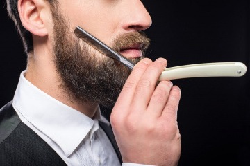 Ein Mann will sich seinen Bart richtig rasieren und stutzt seinen Vollbart dazu zunächst mit einer Bartschere.