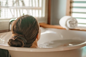 Eine Frau entspannt sich in der Badewanne, nachdem sie erfolgreich gelernt hat, wie man ein Basenbad selber machen kann.