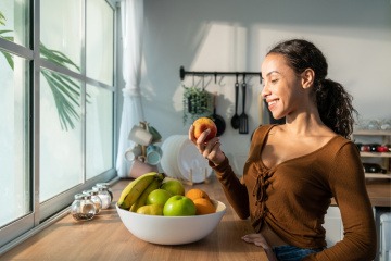 Frau hält Apfel, daneben eine Schüssel mit basischen Mineralstoffen