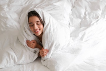 Bett wärmen - Frau eingekuschelt in ihrer warmen Bettdecke.