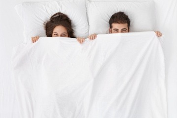 Paar im Bett mit der Bettdecke bis zur Nase