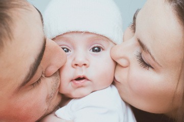 Baby wird von von einem Mann und einer Frau auf jeweils eine Wange geküsst