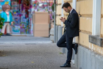 Ein Mann lehnt gedankenverloren an einer Wand und starrt auf sein Handy. 