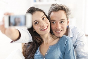 Ein Paar nimmt ein gemeinsames Selfie auf, während es auf einem Sofa sitzt.